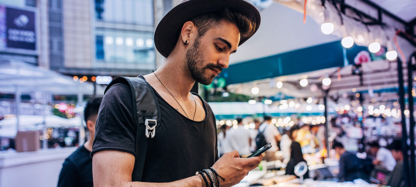 Mann steht mit Handy und Hut in Halle