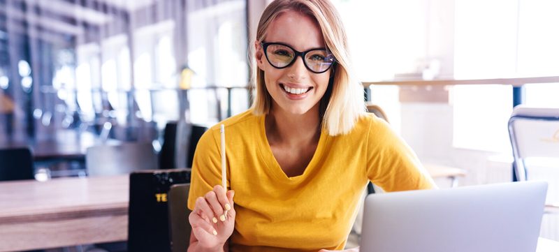 Frau sitzt mit Stift vor Laptop
